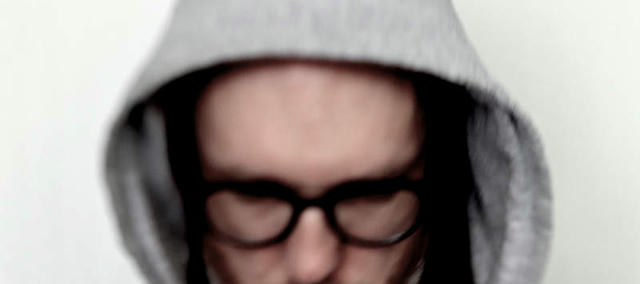 Blurry Photo of the Artist, wearing a hoodie with the hood deep into the face, looking down